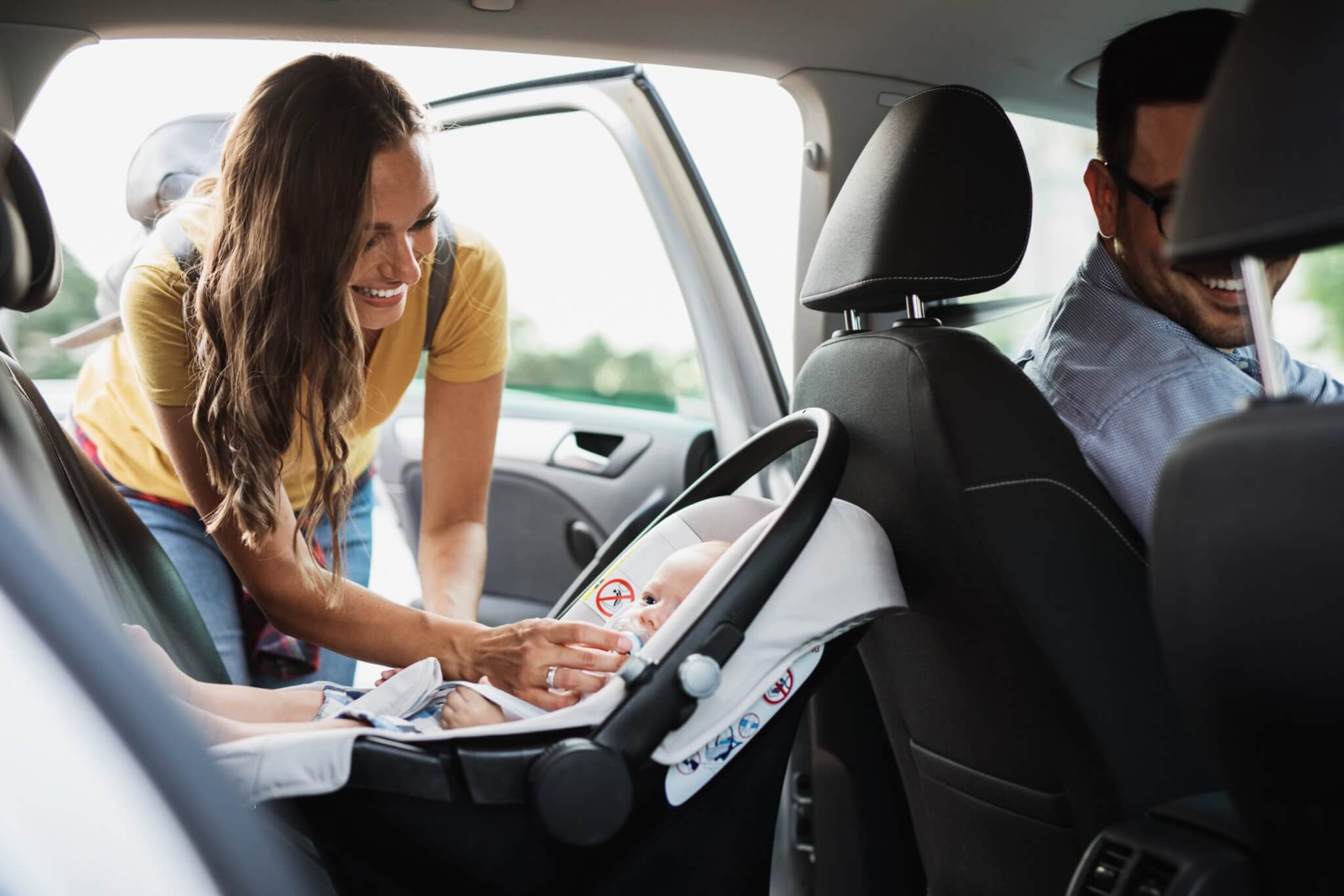 Young mother putting her baby boy on a safety child car seat.