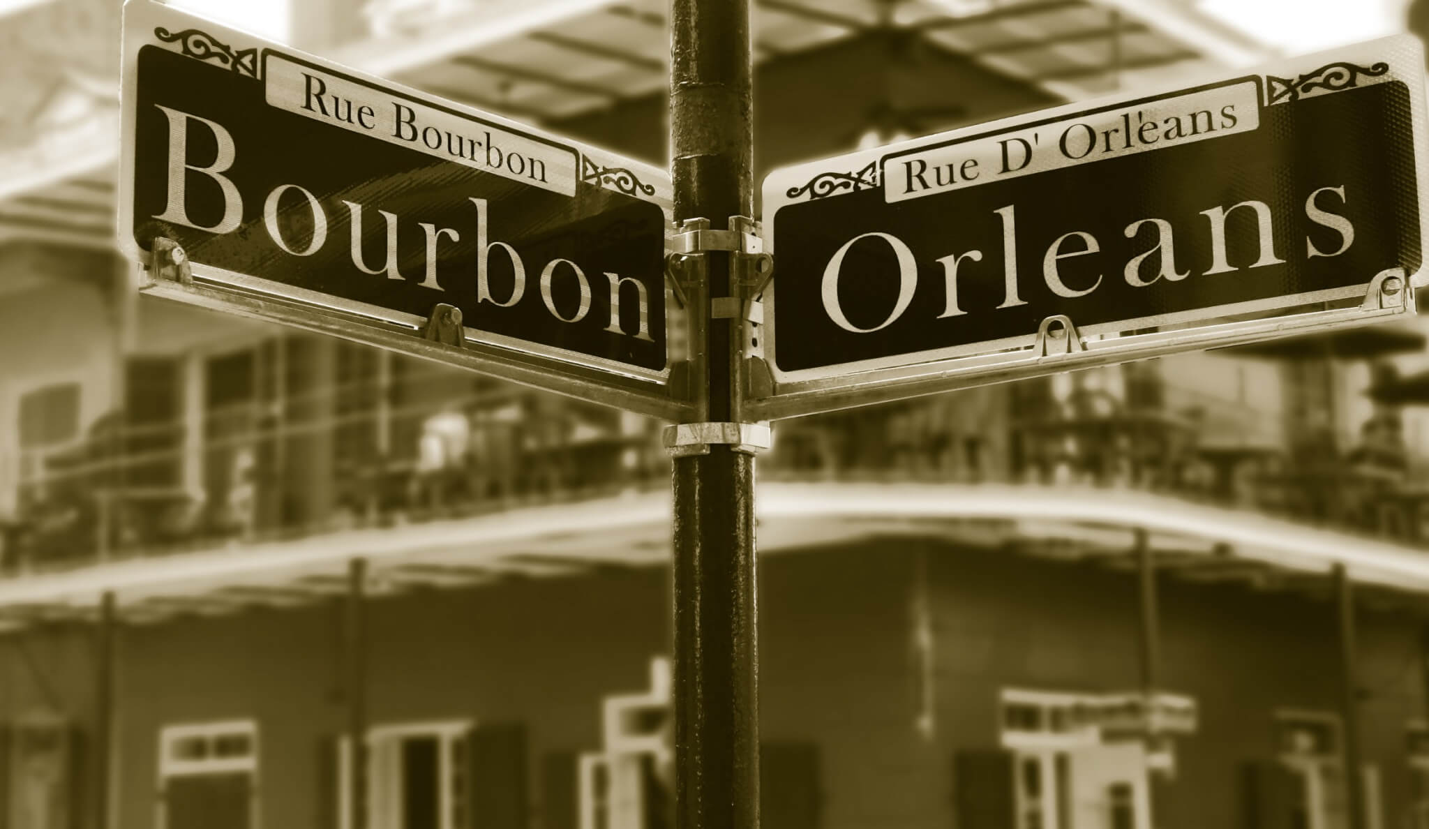 Sepia photo of intersecting street signs for Bourbon Street and Rue d’Orléans in the French Quarter, New Orleans.