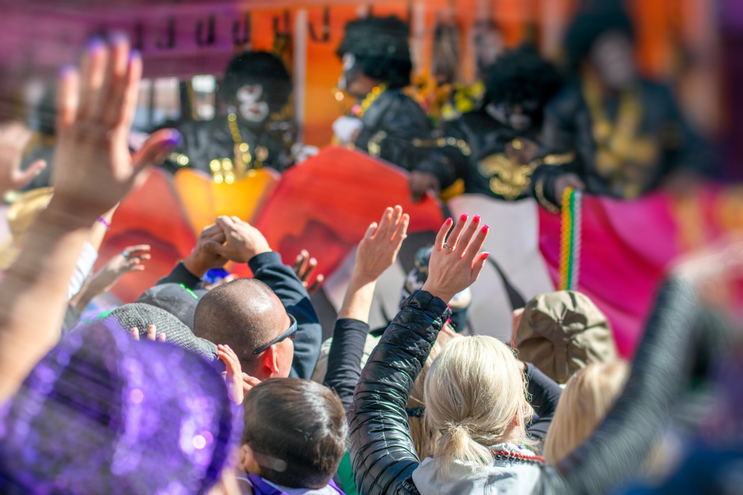 Crowds lining the streets during a Mardi Gras parade in New Orleans, with vibrant floats, costumes, and beads flying through the air.