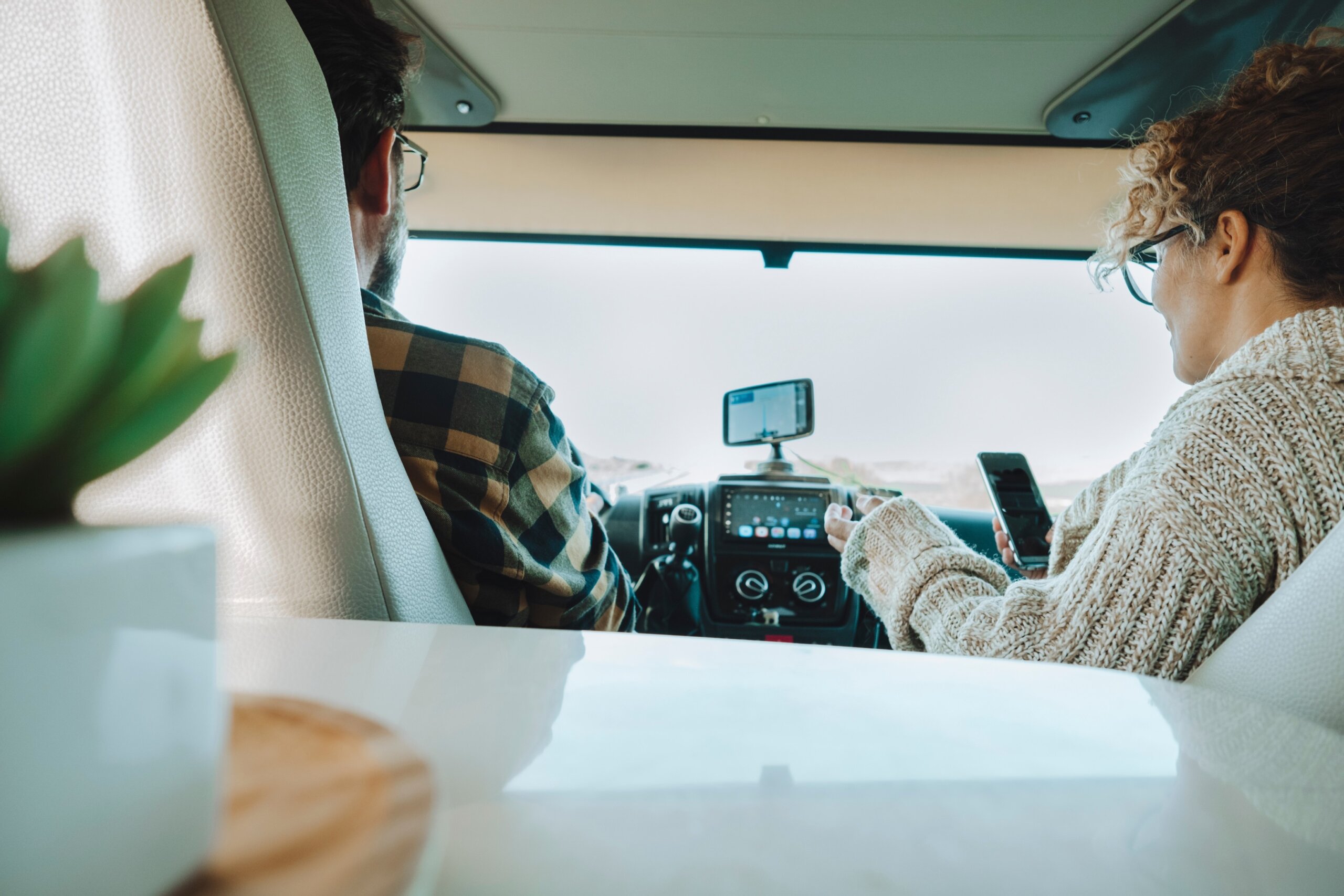 Inside back view of vehicle cabin like motorhome and couple traveling and using gps navigation system and phone to plan road trip and destination.