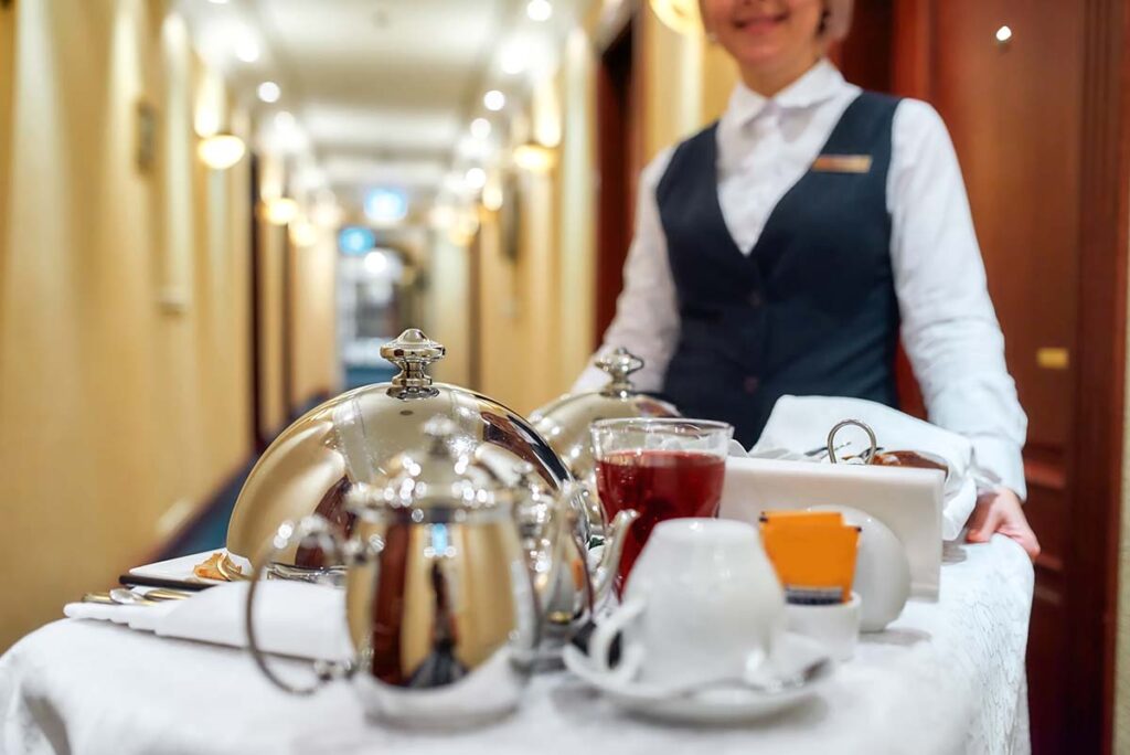 Waitress in uniform delivering tray with food on a cruise ship. Room service.