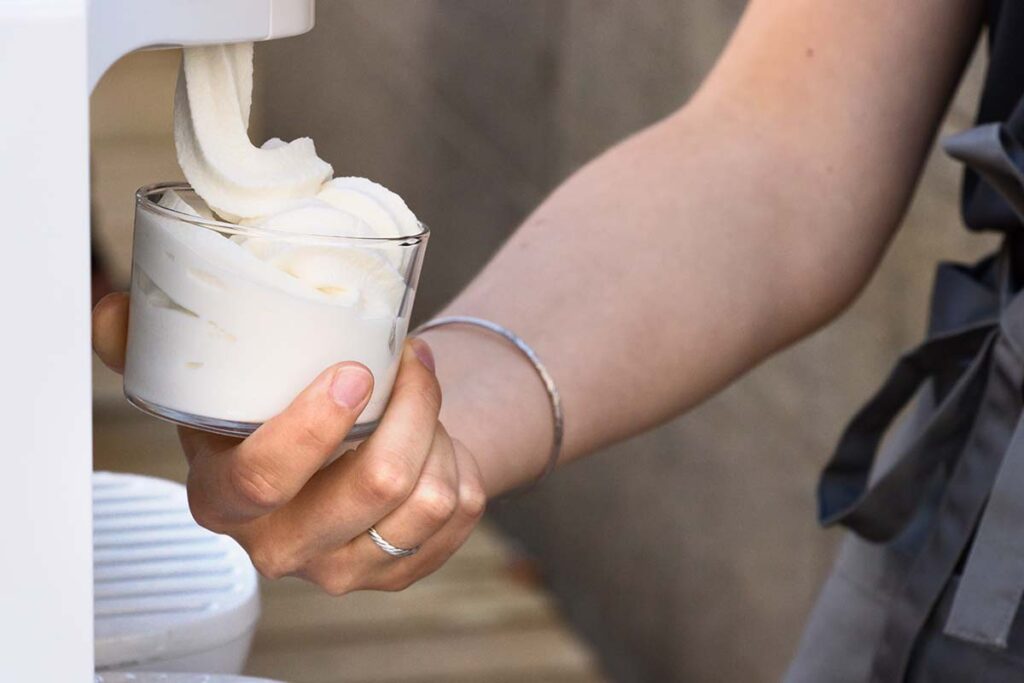 A female hand serving soft ice cream on a glass from a machine.