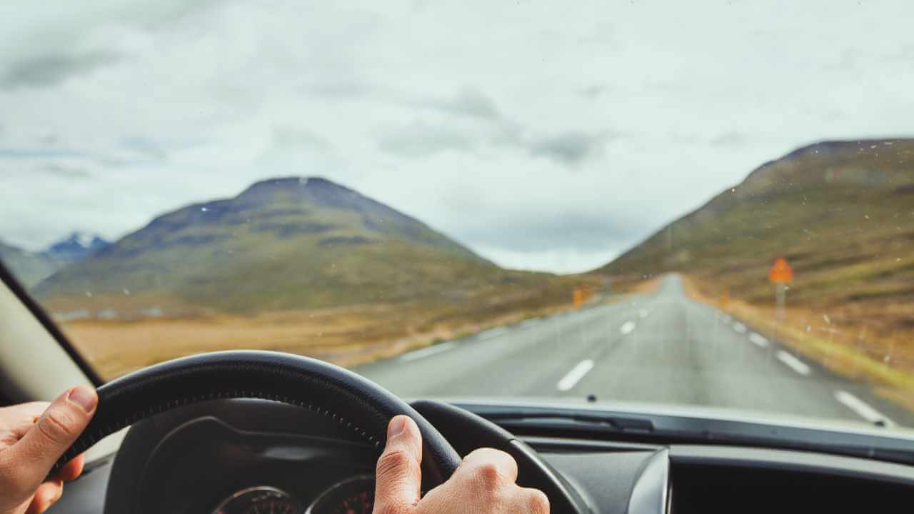 a person driving a car on a road with mountains in the background