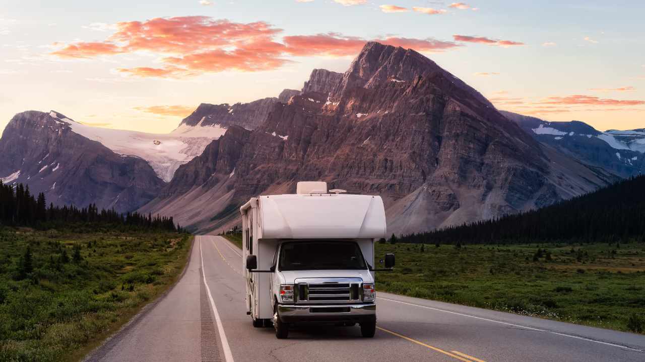 an rv is driving down the road in front of mountains