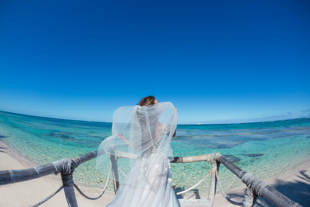 Bride back view in a white wedding dress walking on the sandy caribbean beach landscape on  sunny day in Dominican republic