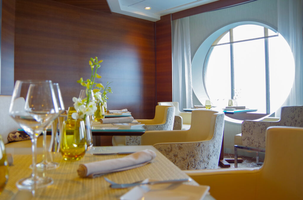 Formal elegant Suite Class restaurant dining room onboard luxury cruiseship or cruise ship liner with set tables, ocean views and impressive interior inside architecture