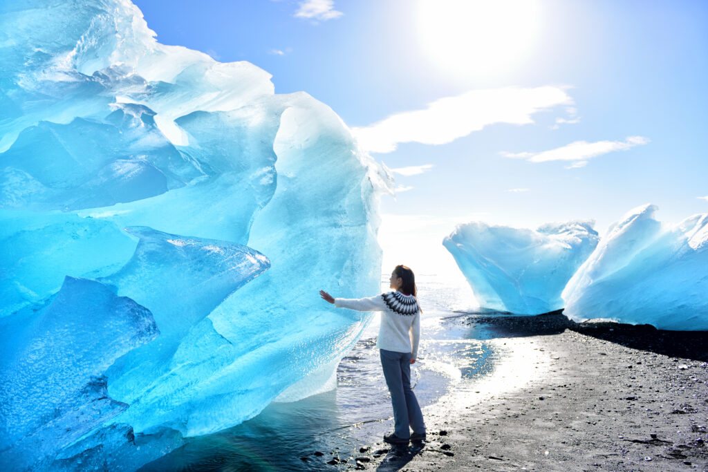 Iceland Amazing landscape at Iceberg beach. Tourist by icebergs on Ice beach, Breidamerkursandur aka Diamond Beach by jokulsarlon glacial lagoon / glacier lake nature. Woman in icelandic sweater.