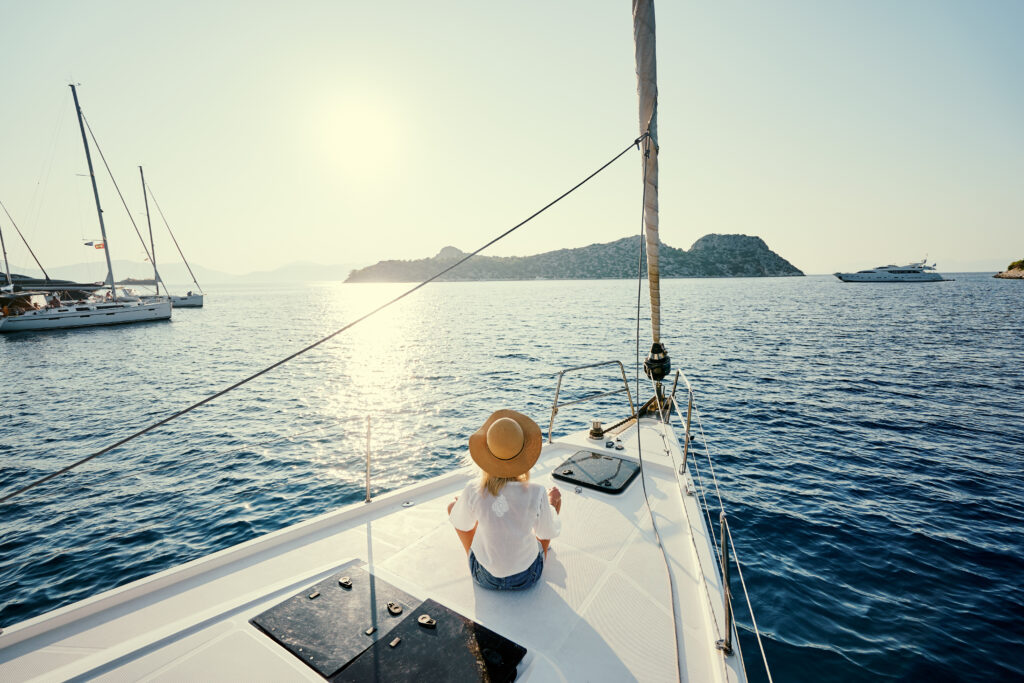 Luxury travel on the yacht. Young happy woman on boat deck sailing the sea. Yachting in Greece.