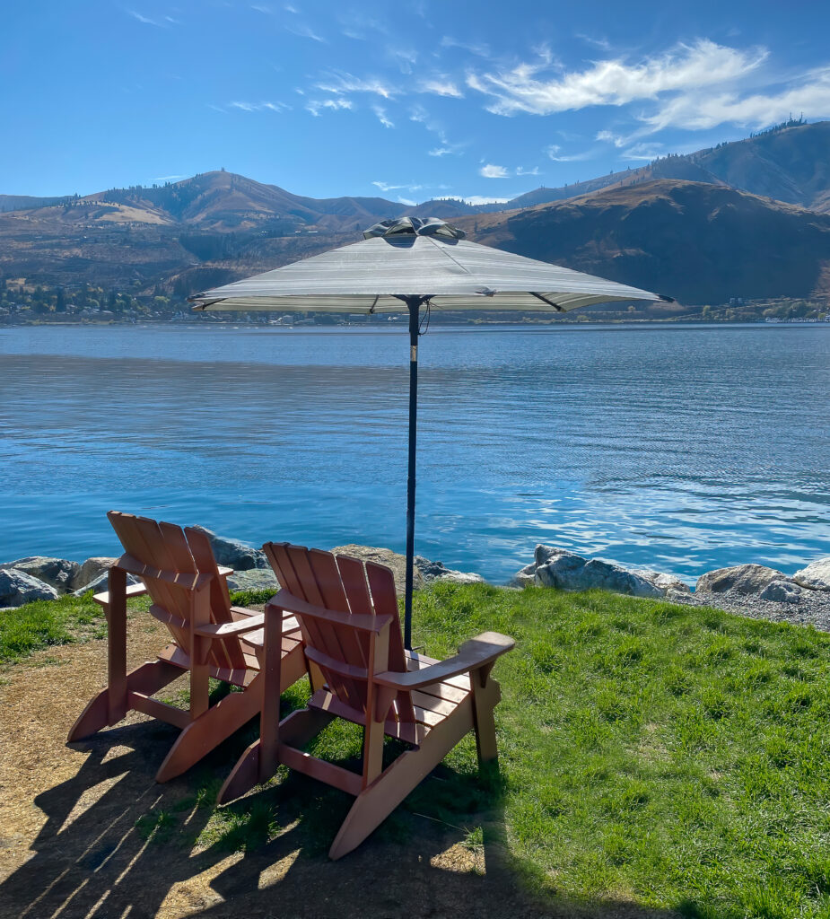 Two empty Adirondack chairs with umbrella on the shores of Lake Chelan Washington on a sunny day