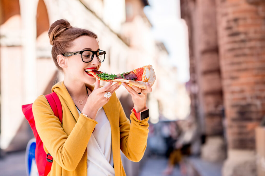 Young female student eating pizza on the break near the university in Bologna city in Italy