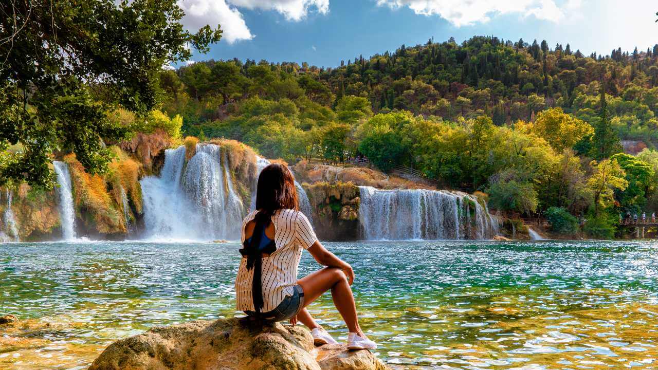 a person sitting on a rock in front of a waterfall