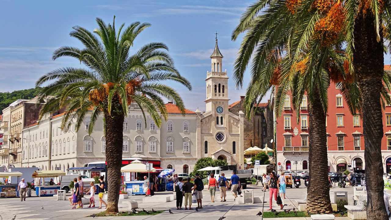 a city square with palm trees and people walking around