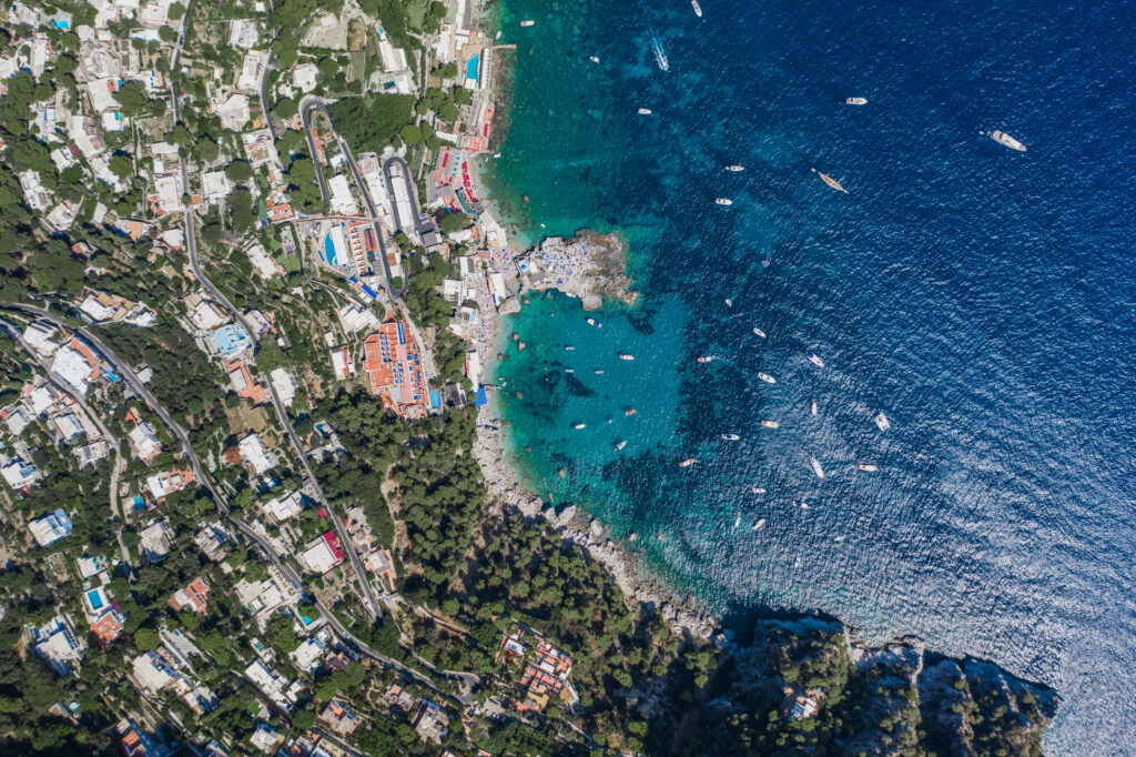 Aerial overhead drone shot of southern Capri Island coastline with yachts in summer noon