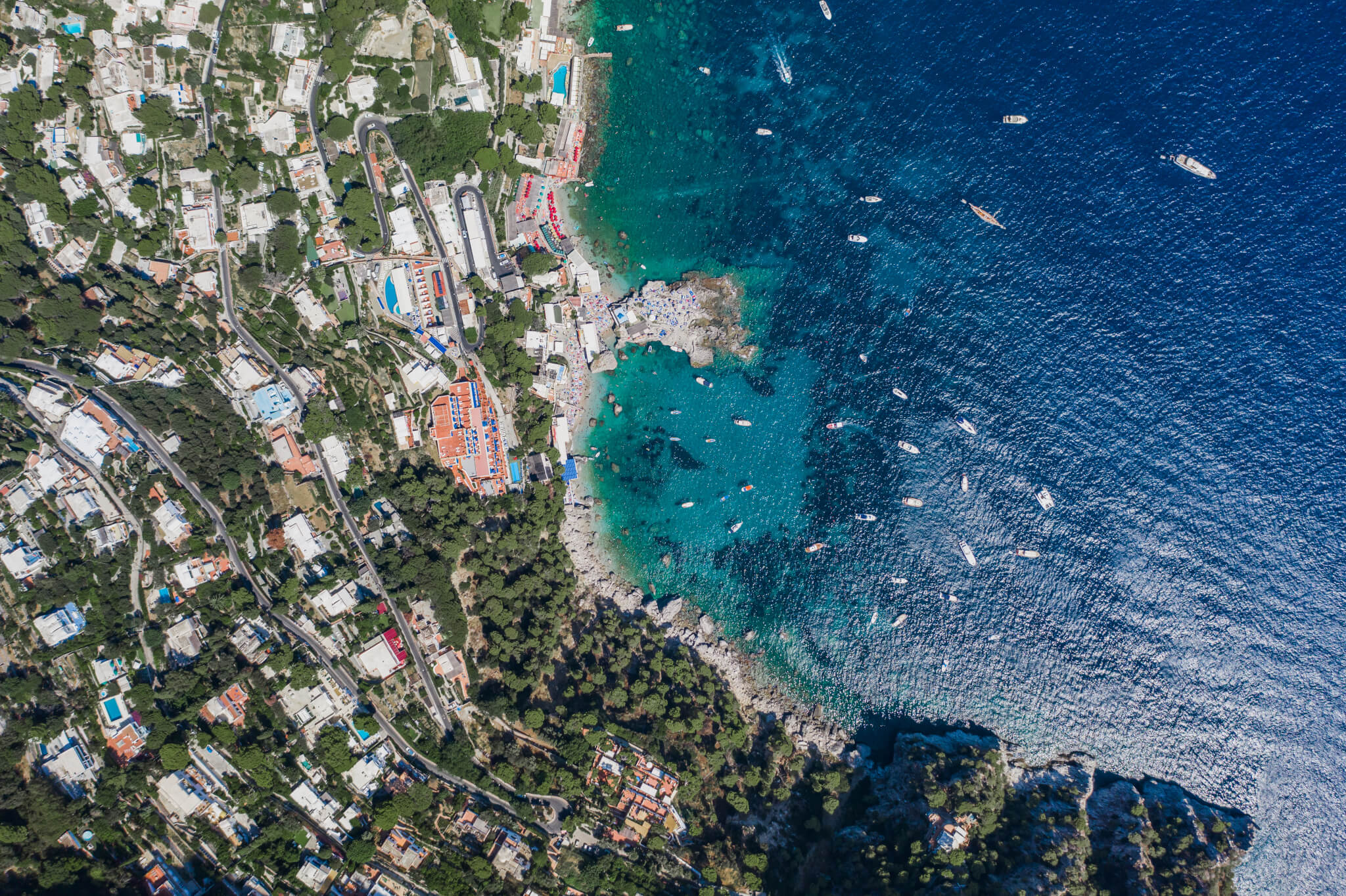 Aerial overhead drone shot of southern Capri Island coastline with yachts in summer noon