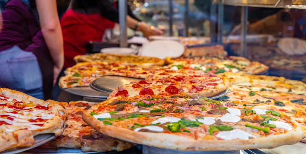 Assortment of italian pizzas in a shop display. Female workers serving the pizzas.