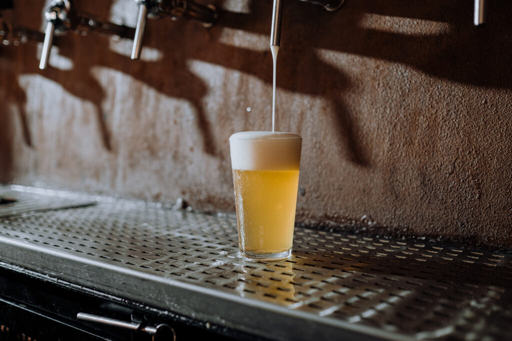 Beer pouring into clear drinking glass on metal surface