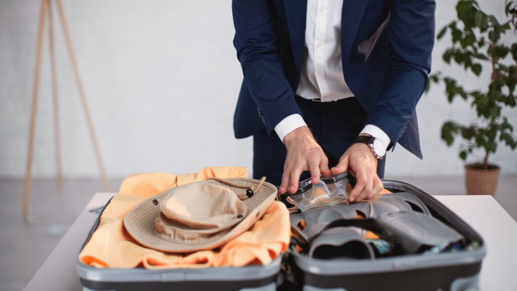 cropped view of businessman in suit packing luggage