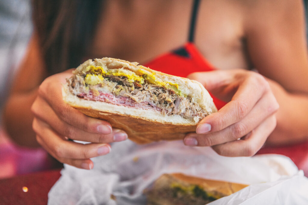 Cuban sandwich closeup woman holding local food at typical cafe outside. Pressed cuban bread with roasted pork, salami sausage, swiss cheese, mustard, typical cuba dish.