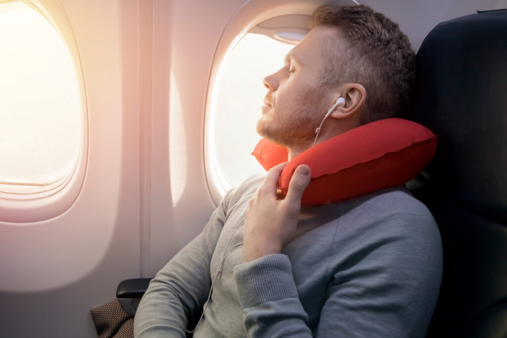 Male passenger of airplane listens to music and enjoys pillow for sleeping in chair.