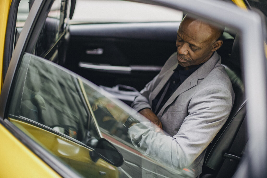 Respectable black businessman sitting in taxi and checking time