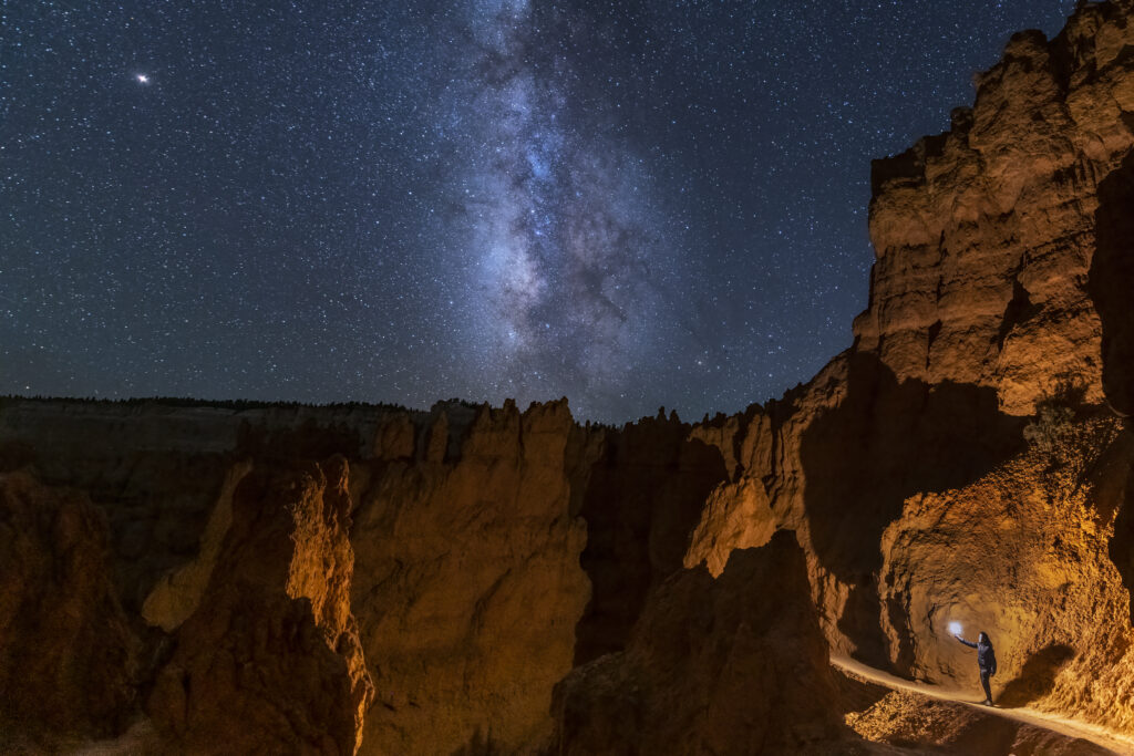 A person holding a light at bryce canyon under a beautiful starry sky