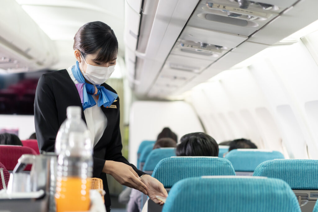 Asian young flight attendant wearing face mask, serving food and drink