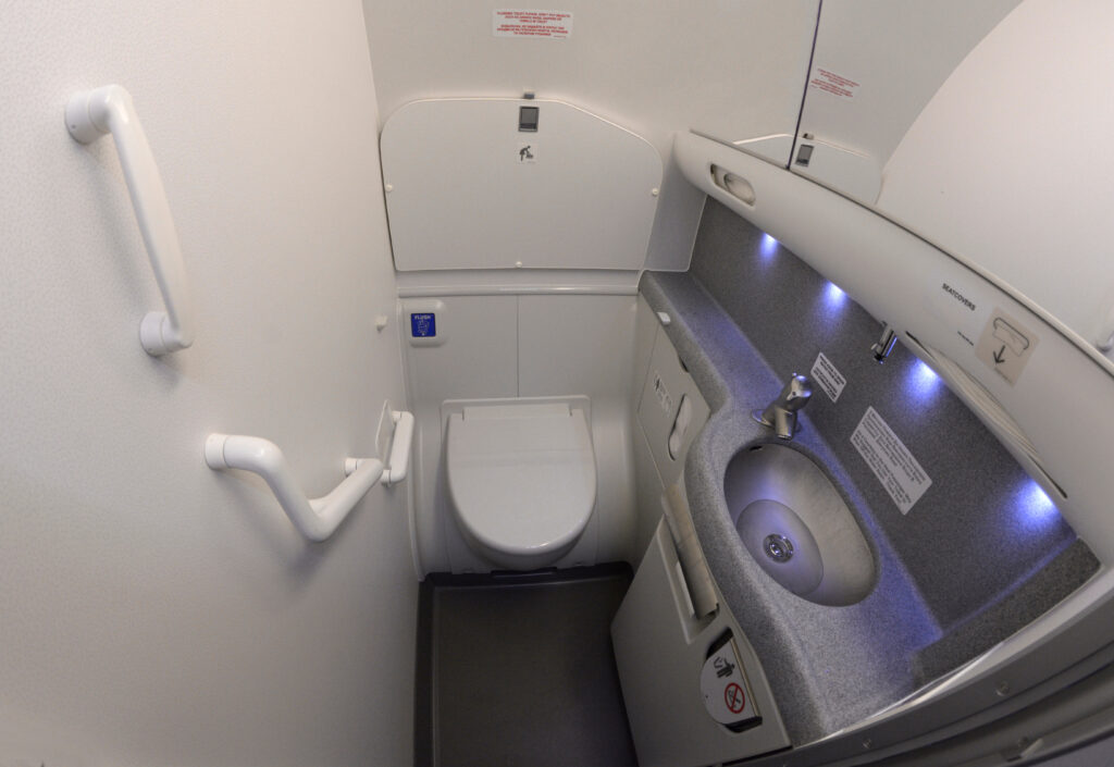 Bathroom of a passenger aircraft Boeing 737. Toilet bowl, sink, knob to drain water, seatcovers, handrails