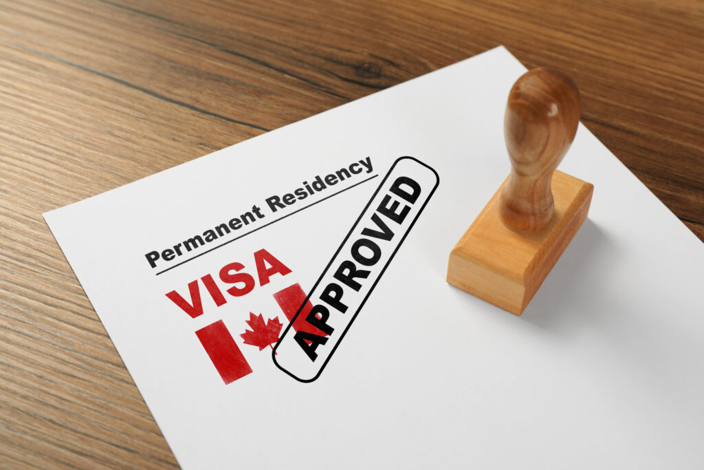 Document with approved permanent residency visa in Canada and stamp on wooden table