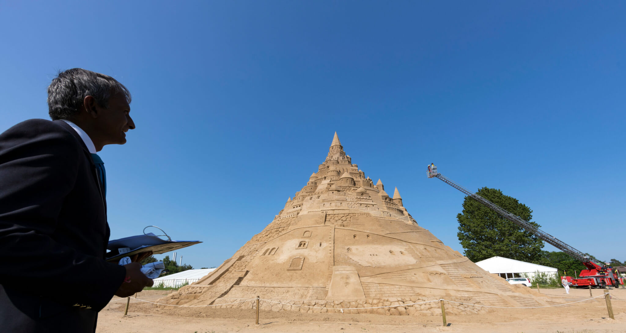 The British record judge Pravin Patel checks a sand castle at the Sand Sculpture Festival in Binz on the island of Ruegen, northern Germany, 05 June 2019. The sculpture is 17.66 meters high and consists of 11,000 tons of sand. The artwork received the 'Greatest Sandcastle in the World' award from Guinness World Records.