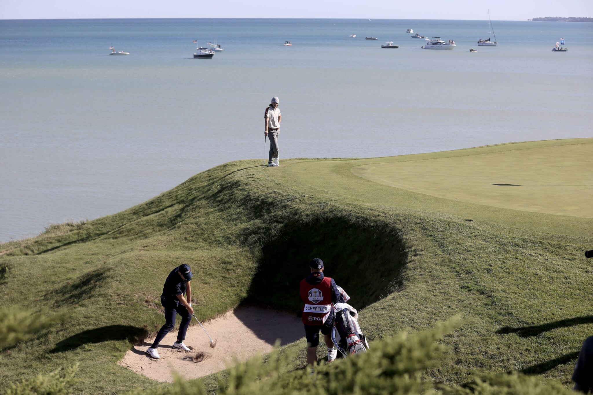 US team member Scottie Scheffler (L) hits out of a bunker on the eighth hole as European team member Tommy Fleetwood of England (Top) looks on during the Four-Ball matches on the pandemic-delayed 2020 Ryder Cup golf tournament at the Whistling Straits golf course in Kohler, Wisconsin, USA, 25 September 2021. Competition for the 43rd Ryder Cup between the US and Europe begins 24 September 2021.
