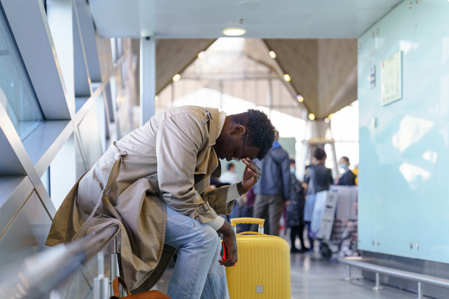 Black young man upset about the cancellation flight. Afro-American traveler male overslept his flight, missed the plane, touching her head, holding cellphone, sitting in airport terminal. 