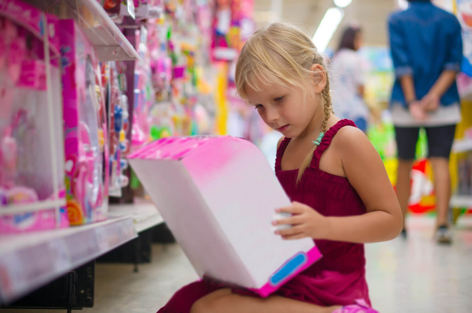Adorable girl selects blue toy dolls on shelves in supermarket