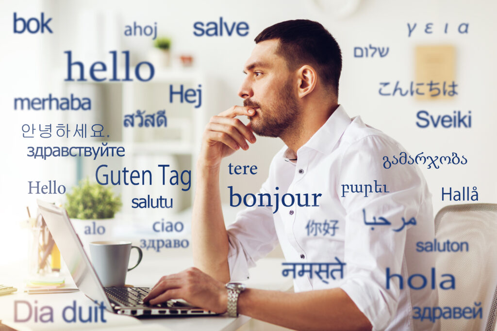 translation, business, and technology concept - male translator or businessman with laptop computer thinking at office over greeting words in different foreign languages