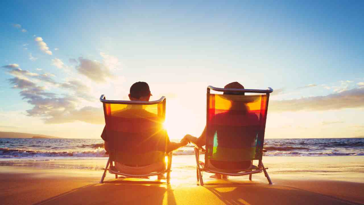 two people sitting in lawn chairs on the beach at sunset