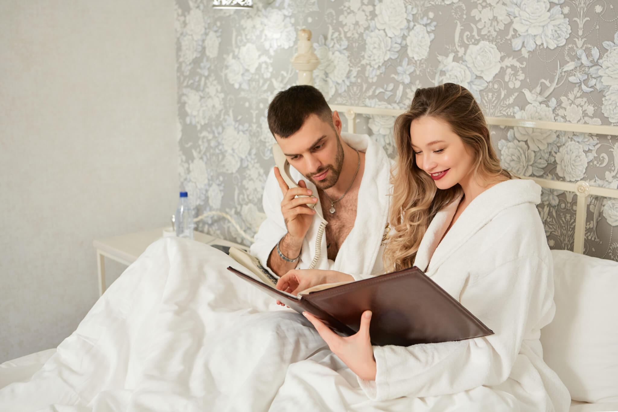 Beautiful couple woke up in bed and makes a phone order from the restaurant menu