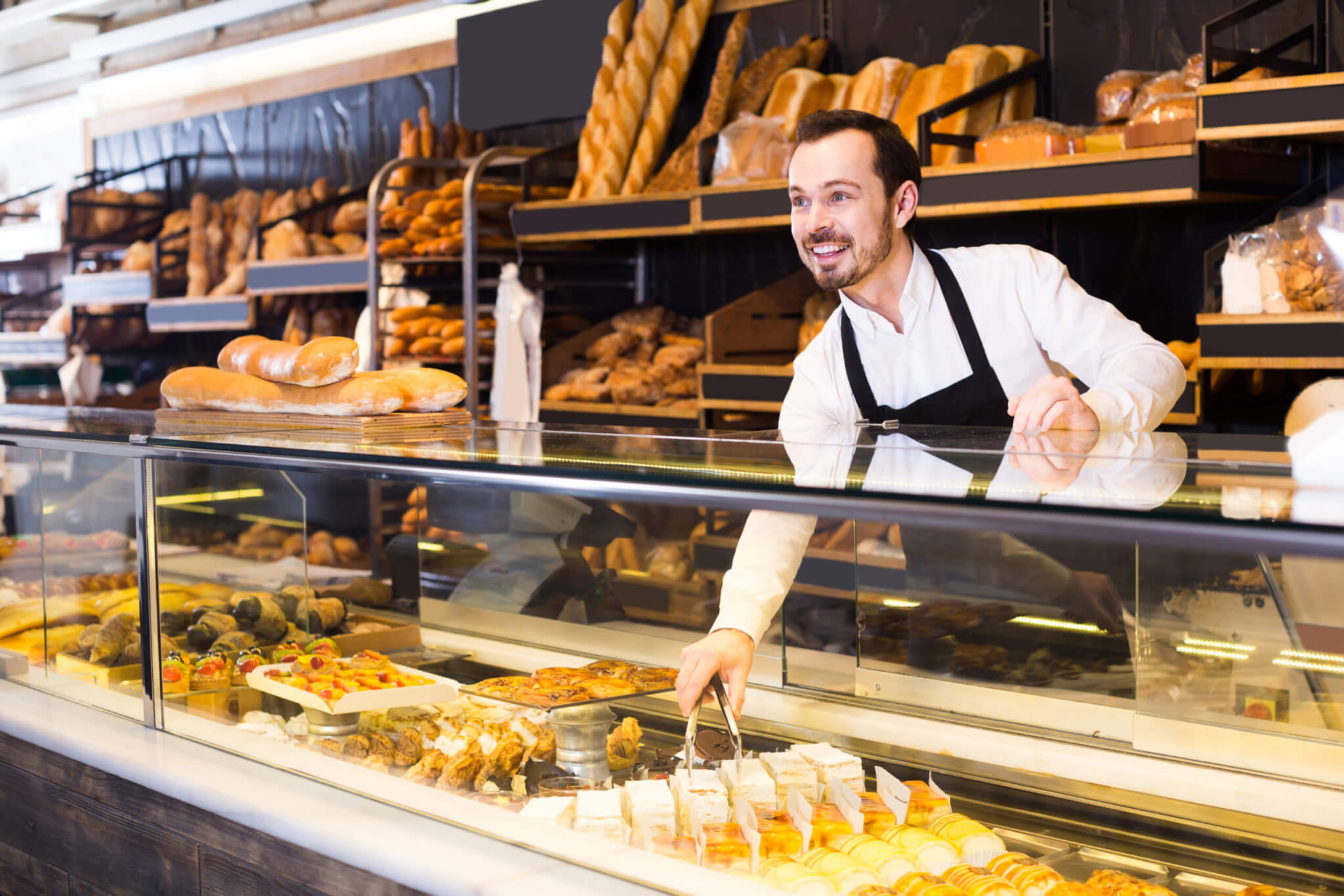 Male shop assistant demonstrating fresh delicious pastry in bakery