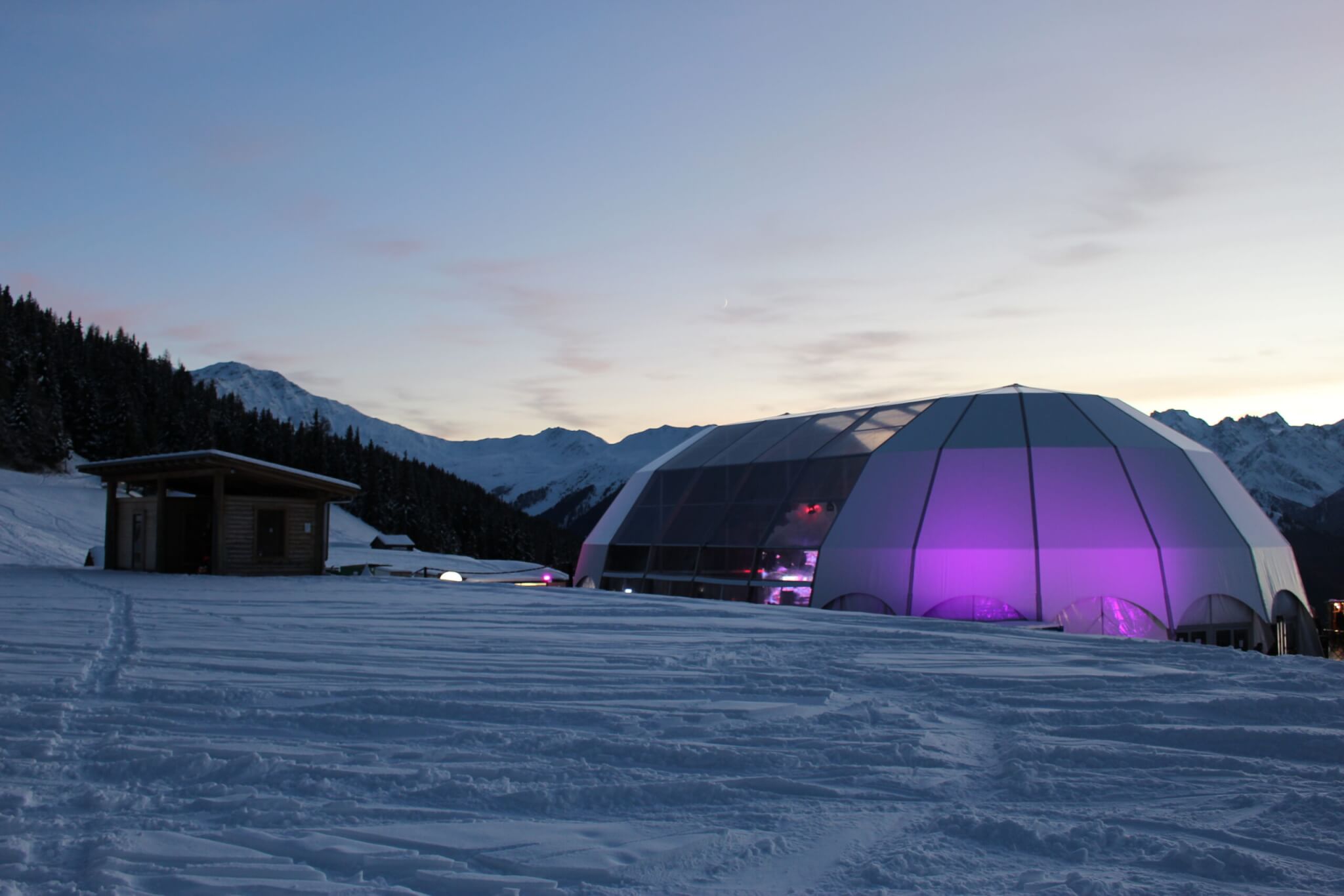 POLARIS FESTIVAL TENT - VERBIER, SWITZERLAND. Built up mountain environment in winter with dome at twilight