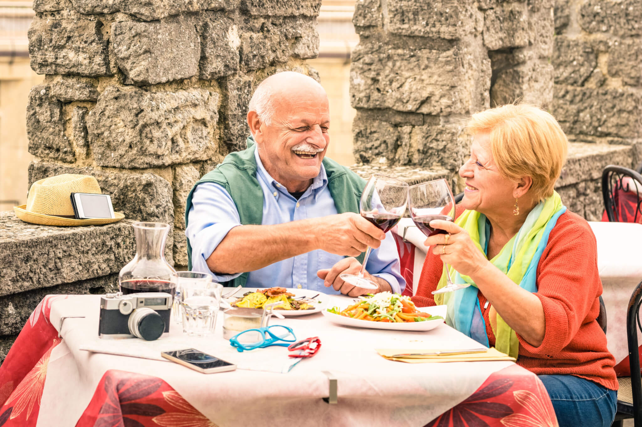 Senior couple having fun eating at restaurant on traveling - Mature man and woman wife on active elderly vacation - Happy retirement concept with retired people together - Warm cloudy day color tones