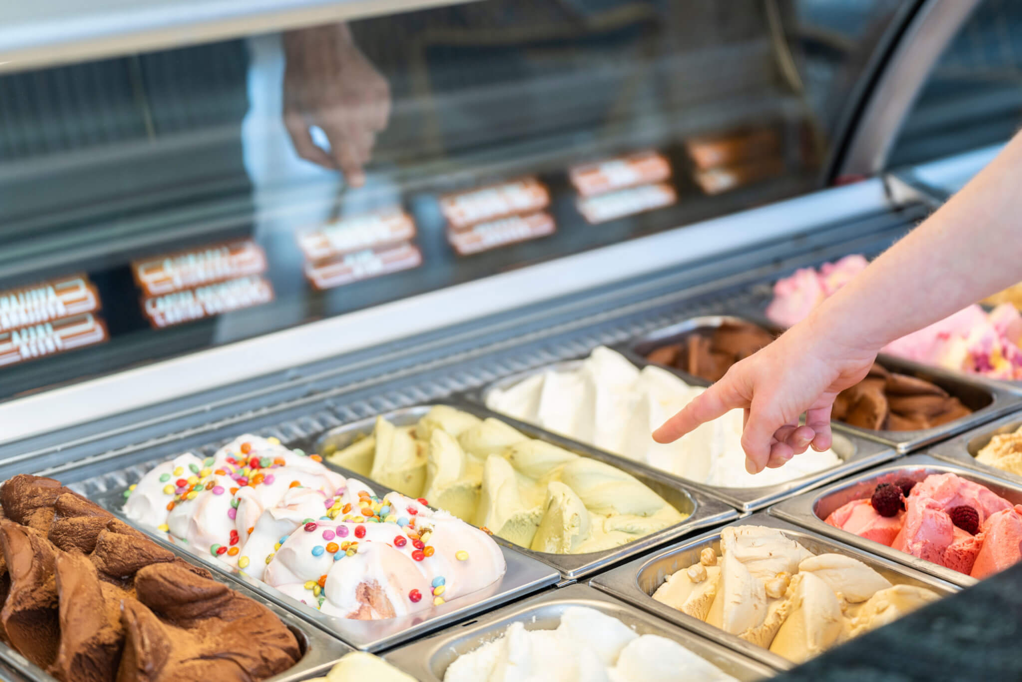 Somebody is choosing a flavor of ice cream in a store with a female assistant