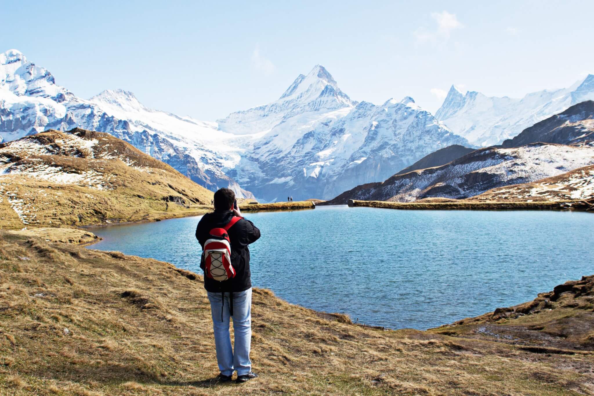 Standing man wearing white and red backpack in front of calm body of water