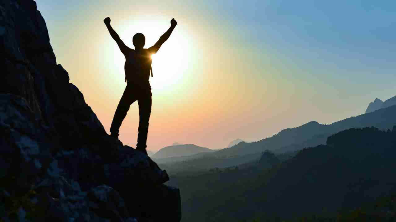 silhouette of a person standing on top of a mountain at sunset