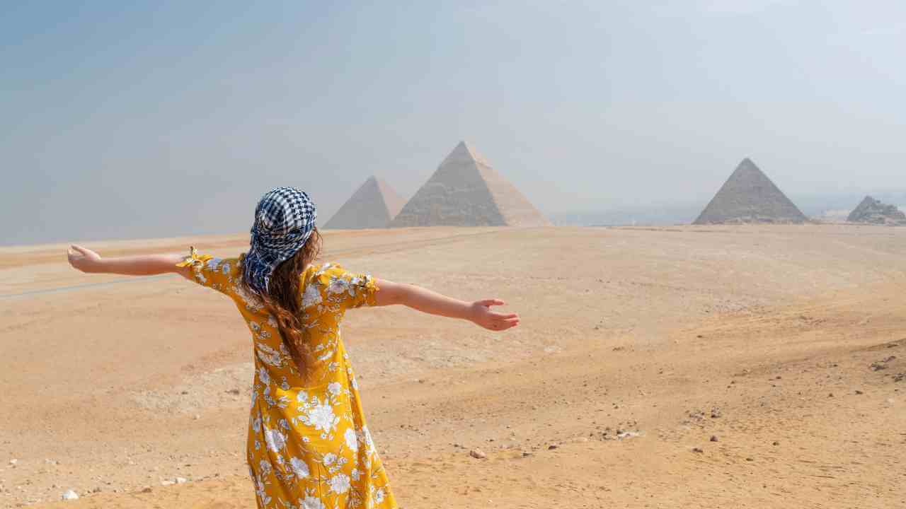 a person in a yellow dress stands in front of the pyramids