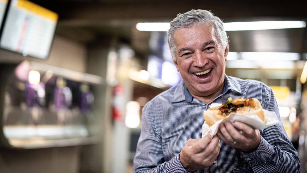 A person is smiling while holding a sandwich