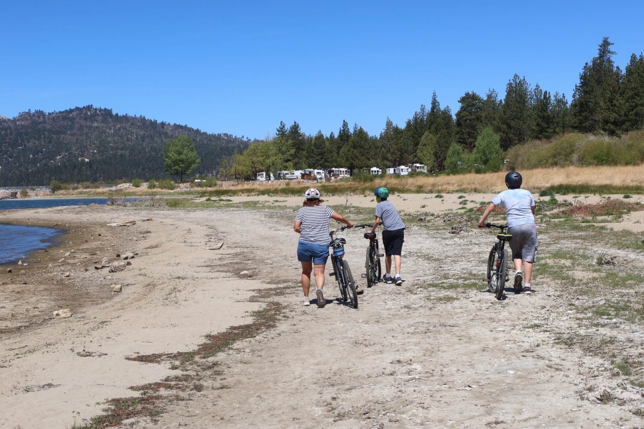 A family Walking their Bikes on a Sandy Beach as they Explore Big Bear Lake, California,