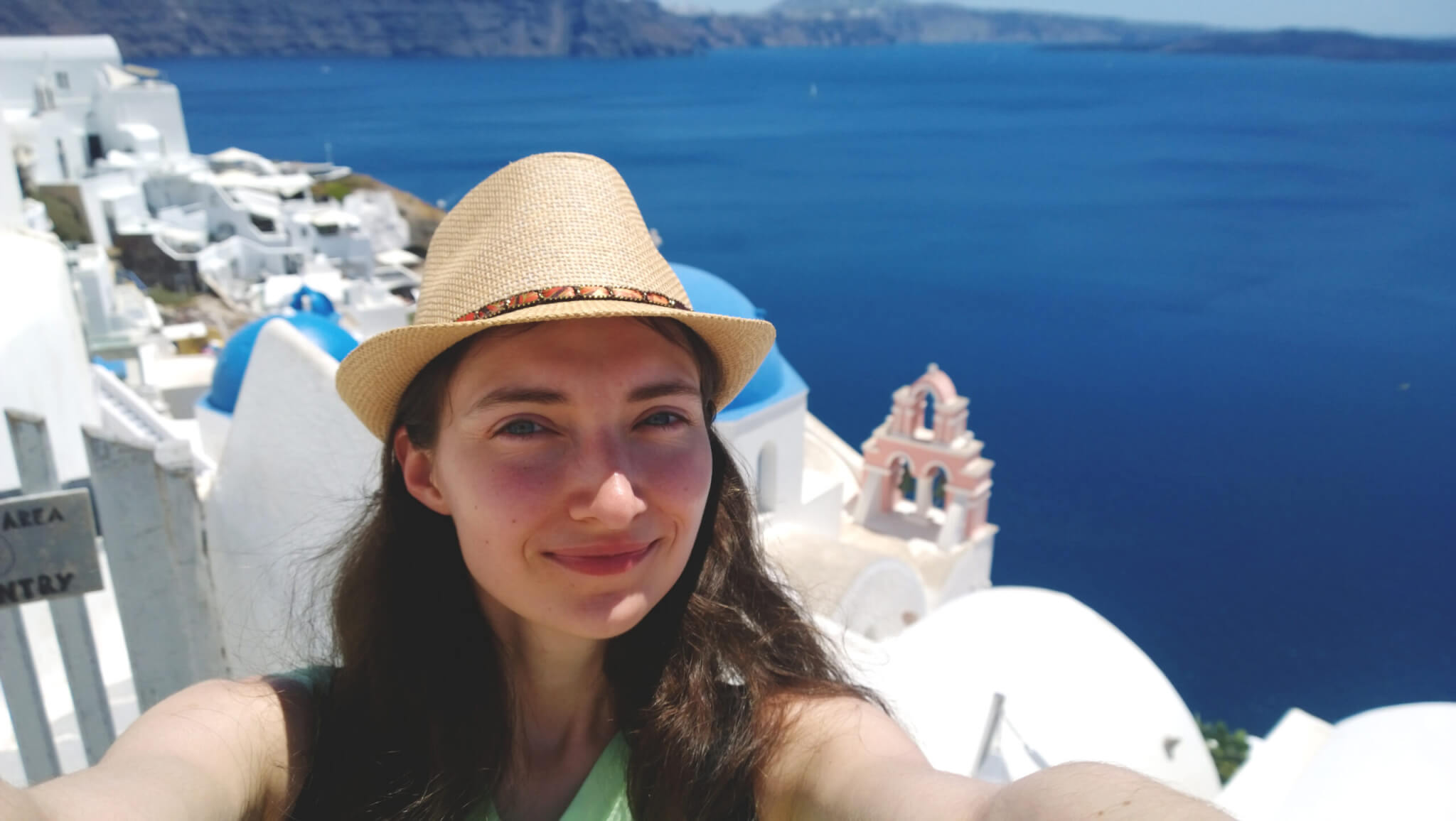 Brunette in straw hat taking a selfie on the background of Oia on Santorini island (Greece)