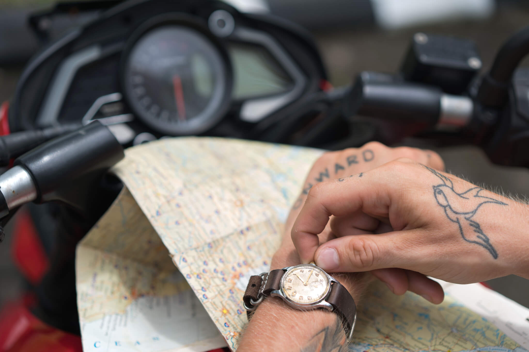 Crop tattooed man setting up watch against map and motorbike