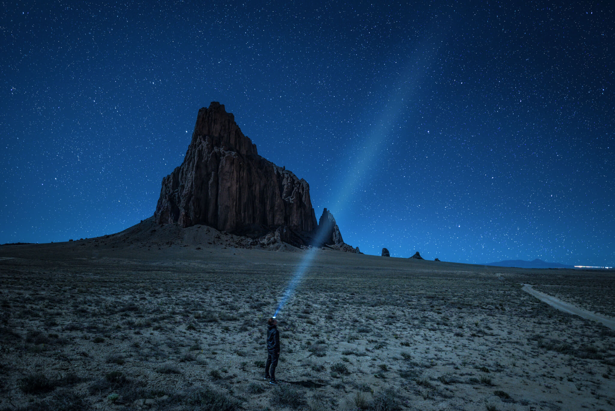 Hiker with a head lamp under the night sky near Shiprock, New Mexico