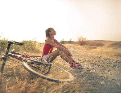 Sportive woman with bicycle resting on countryside road in sunlight