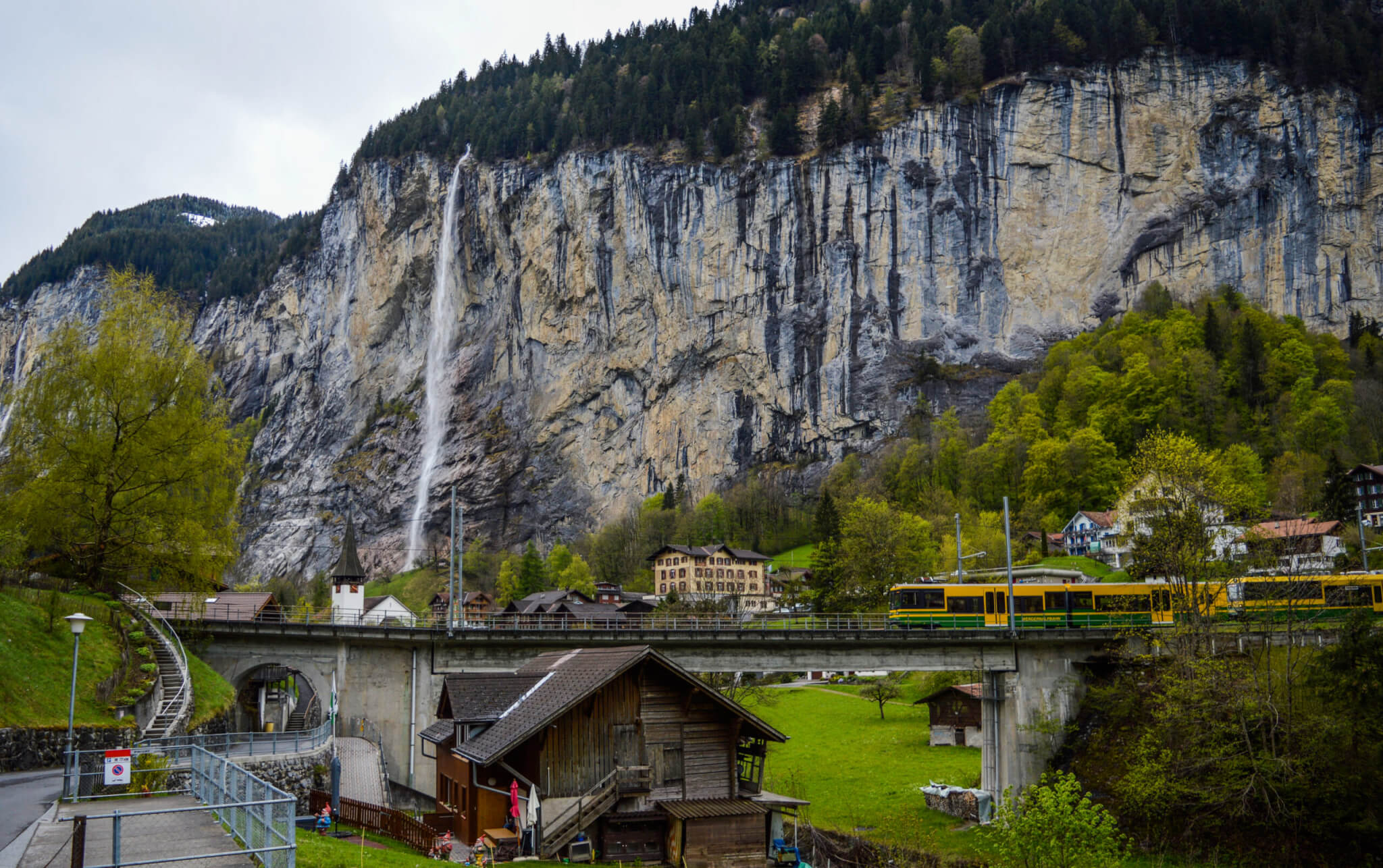 Train riding in mountainous countryside near waterfall flowing through rocky cliff