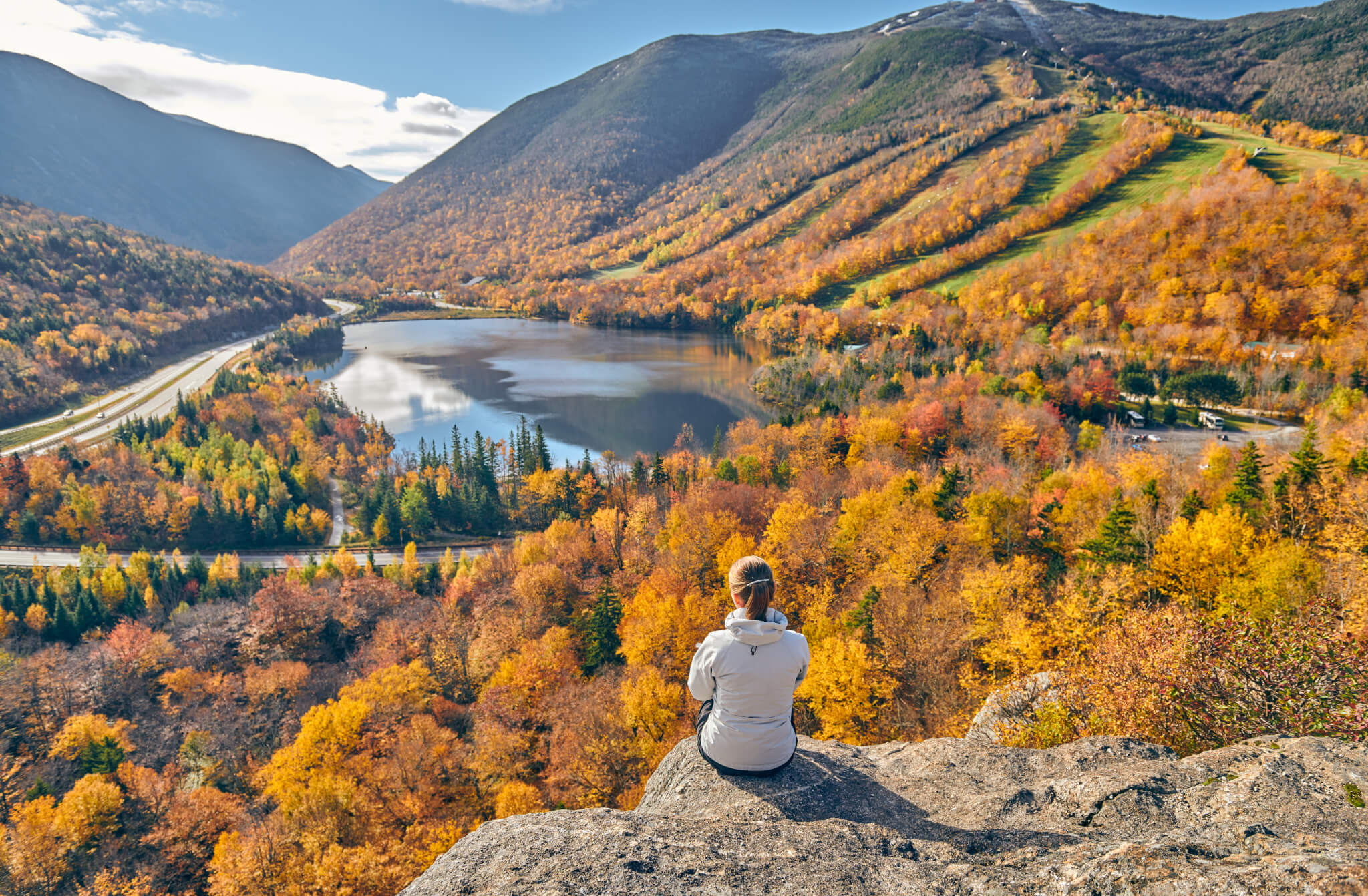 Woman hiking at Artist's Bluff in autumn. View of Echo Lake. Fall colours in Franconia Notch State Park. White Mountain National Forest, New Hampshire, USA